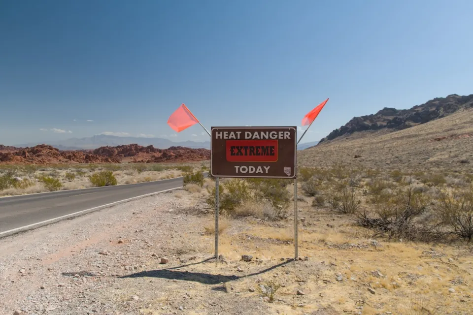 "Heat Danger Extreme Today" sign on desert roadside with orange flags on either side.